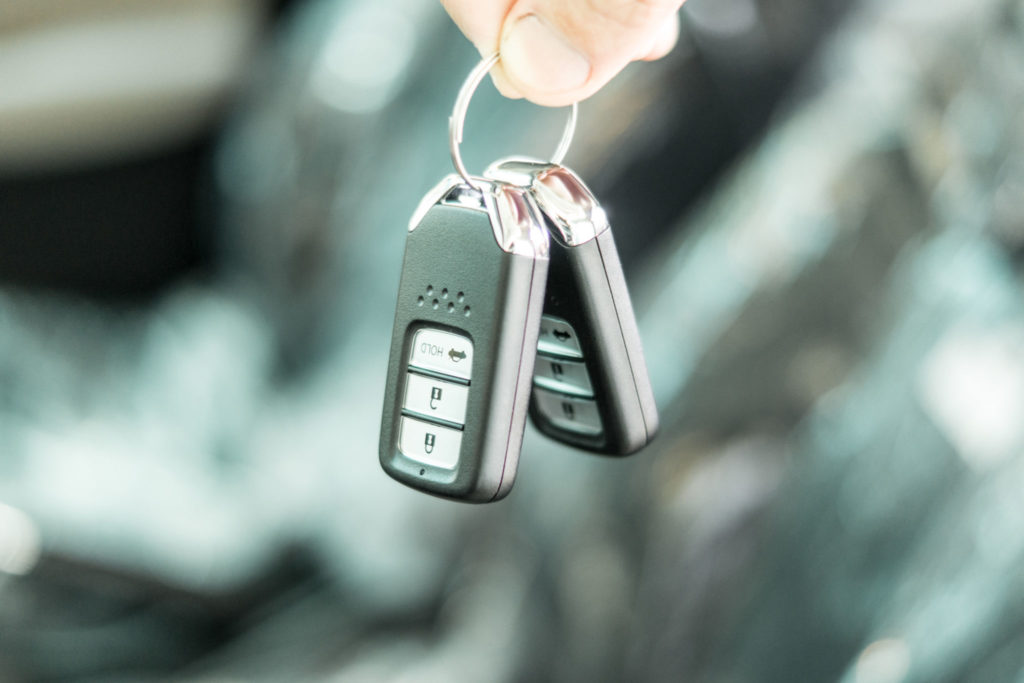 Male holding car key with new car on background, close up.